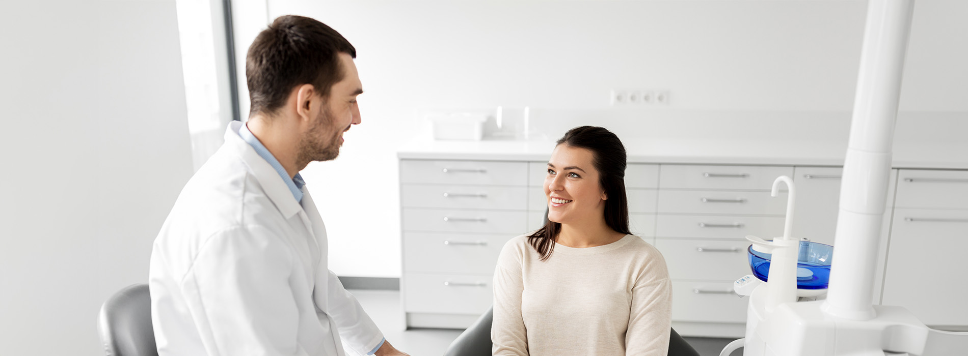 A person is seated in a dental chair, receiving care from a dental professional who stands behind them.